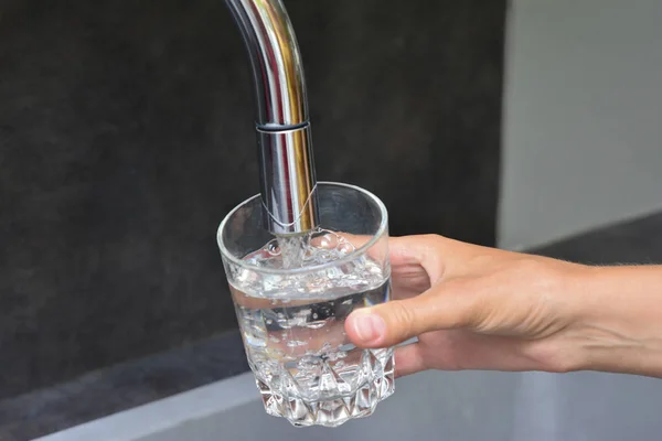 Manos femeninas vertiendo agua en una taza de vidrio — Foto de Stock