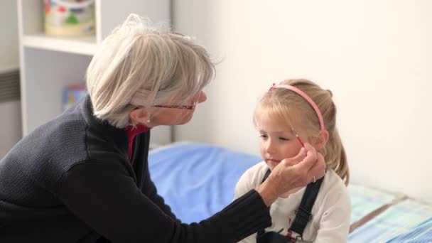 Grand-mère et petite-fille jouent ensemble. Grand-mère peint son visage avec du maquillage pour enfants . — Video