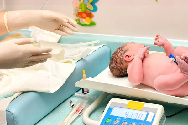 Uma enfermeira pesa nas balanças de um bebê recém-nascido — Fotografia de Stock
