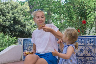 Anne ve kızı Pasteis de Belem yumurtalı tartı yiyorlar. Arkaplanda Azulejos fayansı