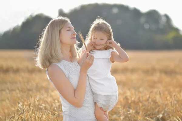 Mother holds daughter in her arms in a field with wheat