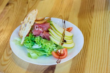 İtalyan salatası prosciutto jambonu, marul, peynir ve elma, güzel bir eski ahşap masaya servis. Seçici odak