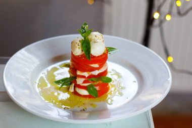 Salata domates ve mozzarella fesleğen ile güzel bir arka plan beyaz bir plaka üzerinde bir kule şeklinde