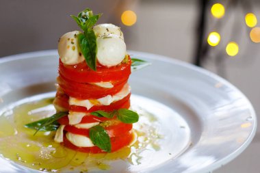 Salata domates ve mozzarella fesleğen ile güzel bir arka plan beyaz bir plaka üzerinde bir kule şeklinde