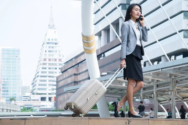 Azjatycki biznes kobieta trzymając telefon komórkowy i holowania bagażu z nowoczesnego miasta na tle, technologii i nowoczesnych koncepcji. — Zdjęcie stockowe