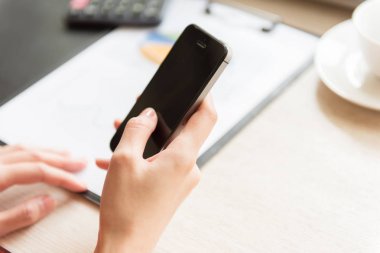 Hesap makinesi ve ahşap masa üzerinde grafik belge ile akıllı telefon elini tutarak iş kadınları kullanın.
