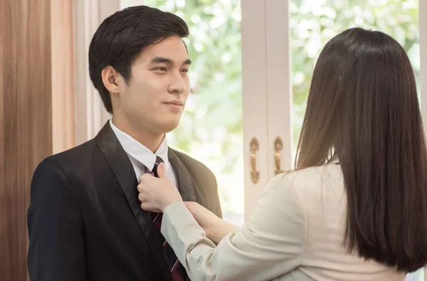 businesswoman tying necktie of businessman near windows.