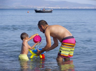 Evia Adası, Yunanistan. Ağustos 2019: Aile: Baba ve oğul bir yaz günü bir Yunan adasında plaja su döküp oynuyorlar