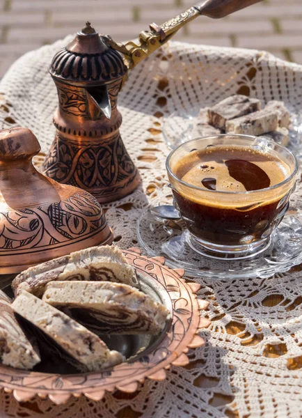 Greek (Turkish) brewed coffee and marble halva on a table with a handmade tablecloth and a copper coffee maker and candy maker on a Sunny day