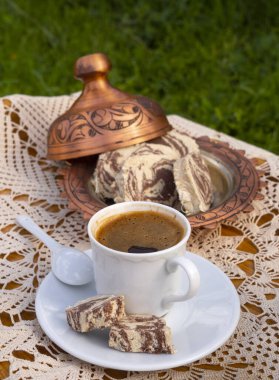 Yunan (Türkçe), güneşli bir günde el yapımı masa örtüsü, bakır kahve makinesi ve şekerleme makinesi bulunan bir masada kahve ve mermer halka demledi