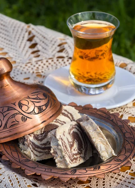 Turkish tea in a glass Cup and marble halva on a table with a handmade tablecloth and candy maker on a Sunny day