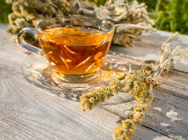 Beautiful glass teacup with Greek mountain herbal (Vounou tea) tea and dried mountain grass Sideritis syriaca on a wooden table in the rays of the setting sun in Greece