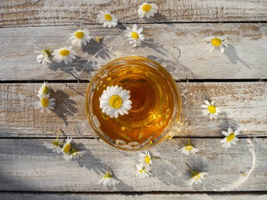 Yunanistan 'da batan güneşin ışınlarında açan papatyaların arasında, ahşap bir masanın üzerinde papatya çayıyla güzel bir cam çay fincanı.