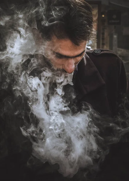 Bir adam elini tutuyor ve elektronik bir sigara içiyor. VAPE ve buhar bulutları salıyor.)