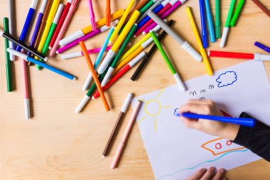 Hareketi ile ahşap masa üzerinde renkli işaretleme kalemleri ile çizim çocuk