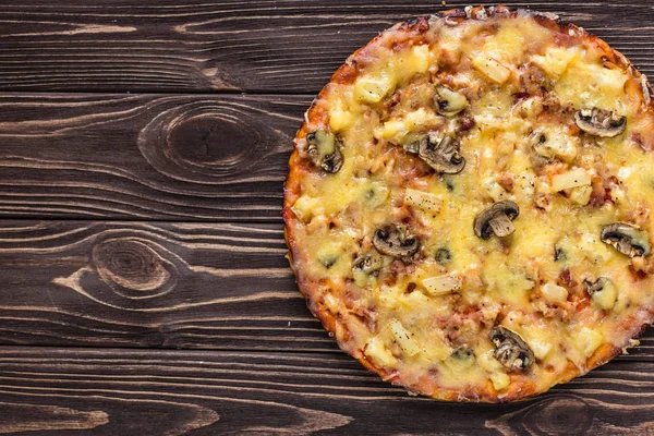 Hawaiian pizza with meat, mushrooms and pineapple on a wooden background