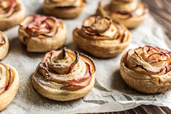 Apple rose puff pastries sprinkled with powdered on baking paper — Stock Photo, Image