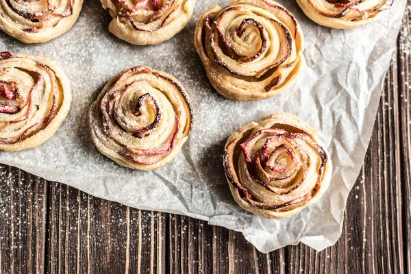 Apple rose puff pastries sprinkled with powdered on baking paper — Stock Photo, Image