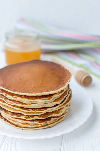 Desayuno saludable. Montón de deliciosos panqueques caseros con miel en plato blanco sobre fondo de madera — Foto de Stock