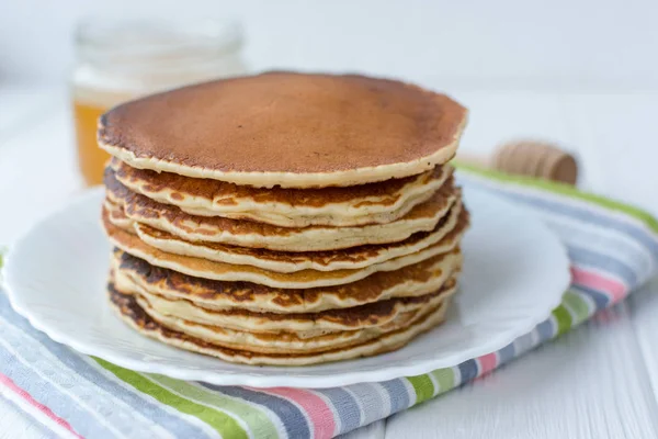 Desayuno saludable. Montón de deliciosos panqueques caseros con miel en plato blanco sobre fondo de madera — Foto de Stock