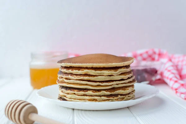 Desayuno saludable. Montón de deliciosos panqueques caseros con miel en plato blanco sobre fondo de madera — Foto de Stock