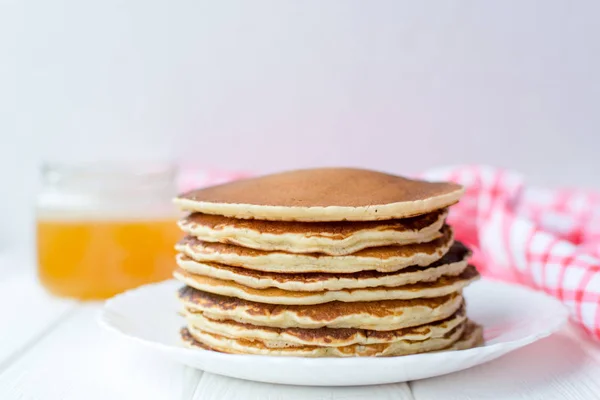 Desayuno saludable. Montón de deliciosos panqueques caseros con miel en plato blanco sobre fondo de madera — Foto de Stock