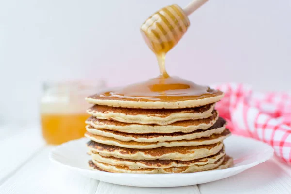 Desayuno saludable. Montón de deliciosos panqueques caseros con miel en plato blanco sobre fondo de madera — Foto de Stock