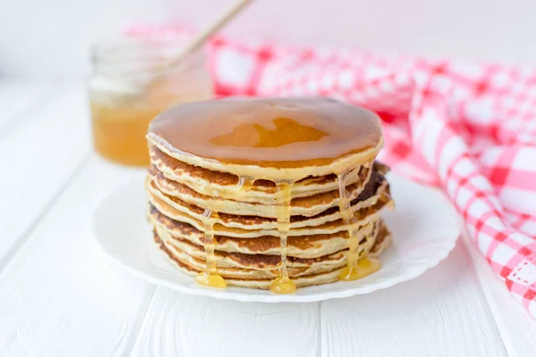 Desayuno saludable. Montón de deliciosos panqueques caseros con miel en plato blanco sobre fondo de madera — Foto de Stock