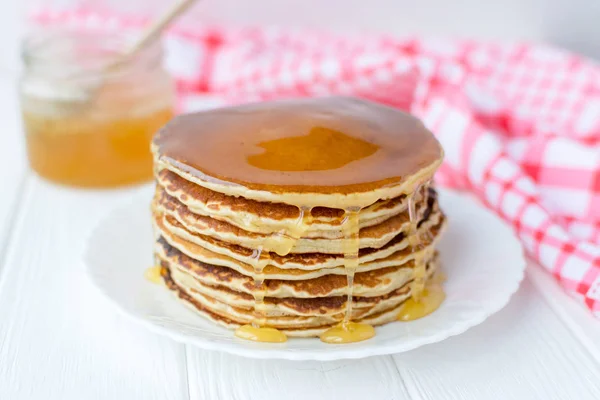 Desayuno saludable. Montón de deliciosos panqueques caseros con miel en plato blanco sobre fondo de madera — Foto de Stock