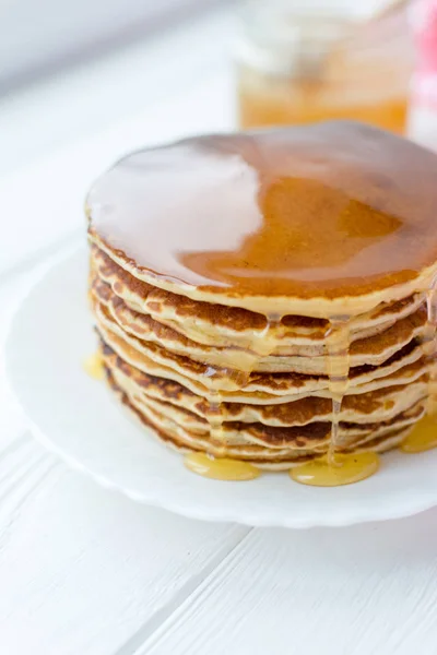 Здоровый завтрак. Стопка вкусных домашних блинчиков с медом на белой тарелке на деревянном фоне — стоковое фото