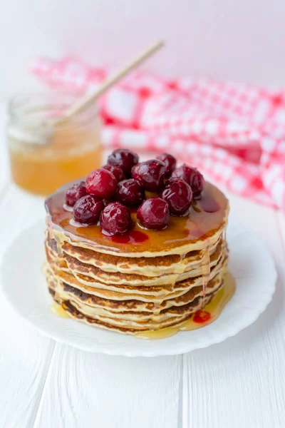 Sarapan sehat. Setumpuk pancake buatan sendiri yang lezat dengan madu dan ceri di atas piring putih — Stok Foto