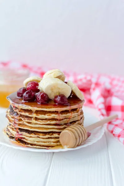 Pequeno-almoço saudável. Pilha de deliciosas panquecas caseiras com mel, cereja e banana no prato branco — Fotografia de Stock