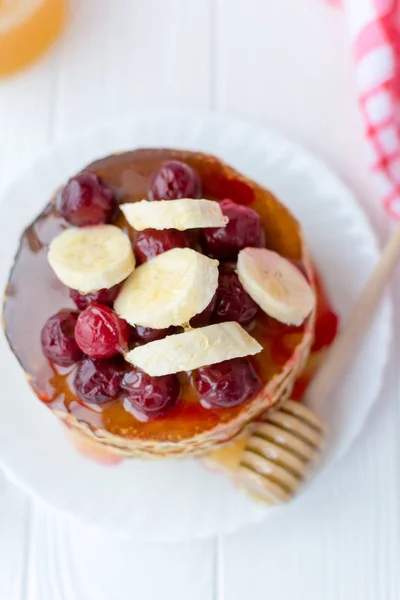 Pequeno-almoço saudável. Pilha de deliciosas panquecas caseiras com mel, cereja e banana no prato branco — Fotografia de Stock