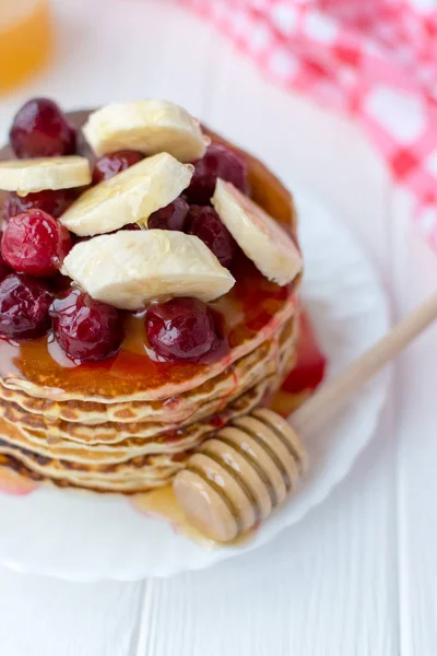 Egészséges reggeli. Verem, a finom, házi készítésű palacsintát, mézzel, cseresznye és banán, fehér lemez — Stock Fotó