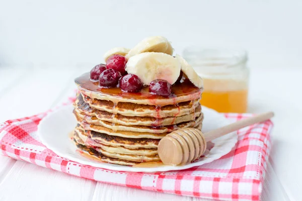 Egészséges reggeli. Verem, a finom, házi készítésű palacsintát, mézzel, cseresznye és banán, fehér lemez — Stock Fotó