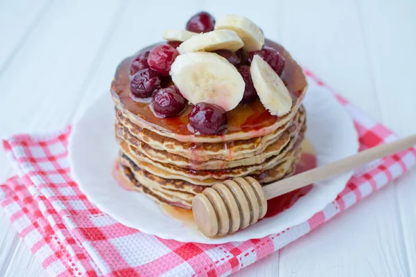 Healthy breakfast. Stack of delicious, homemade pancakes with honey, cherry and banana on white plate — Stock Photo, Image