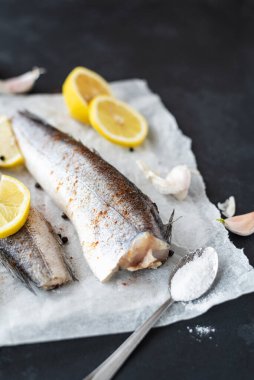 Siyah arka planda taze çiğ hake fileto. Limonlu taze balık, sarımsak, kaşıkta tuz ve biber karışımı.