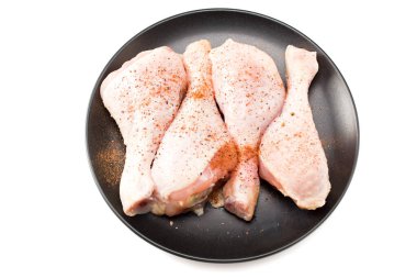 Siyah tabakta çiğ tavuk bacağı, beyaz arka planda izole.