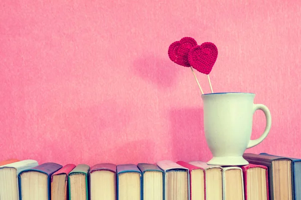 Cup with red crochet hearts on books — Stock Photo, Image