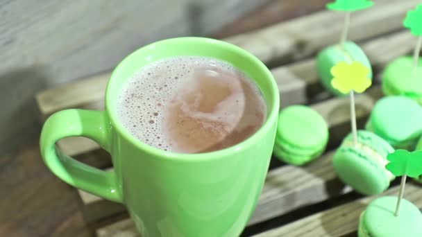 Zöld csésze a forró csokoládé és zöld macaroons lóherék attribútumokkal át a hangsúly. Lassú mozgás. — Stock videók