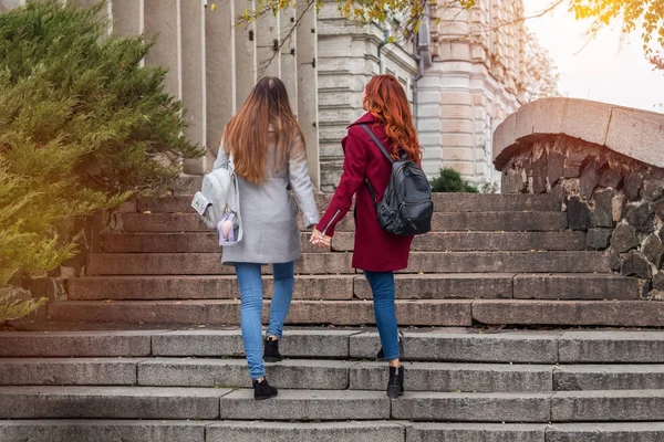Дві жінки-підлітки піднімаються на кам'яні сходи, тримаючись за руки — стокове фото