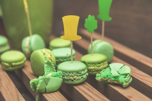 Green macaroon cookies scattered on the wooden surface with St. — Stock Photo, Image