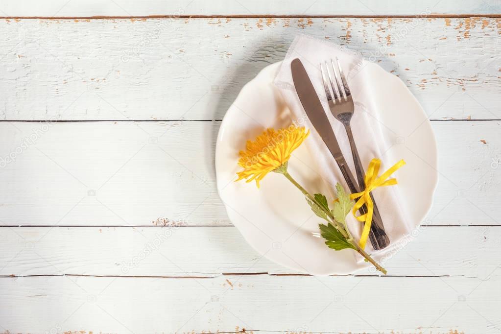 White empty plate, yellow chrysanthemum flowers, napkin, fork an