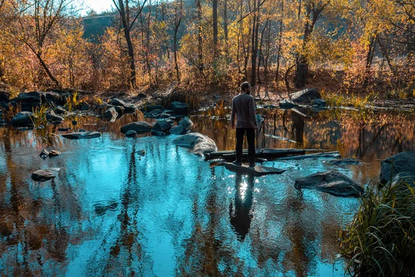 Молодий чоловік біжить через річку на скелі. Дивовижні дерева відображення — стокове фото
