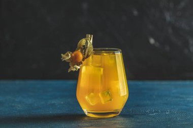 Mandalinalı sarı turuncu kokteyl ve cam kaplı biberiye koyu mavi beton arka planda Physalis Peruviana, yakın plan. Noel ve Yeni Yıl Tatili Hoş geldin içkisi