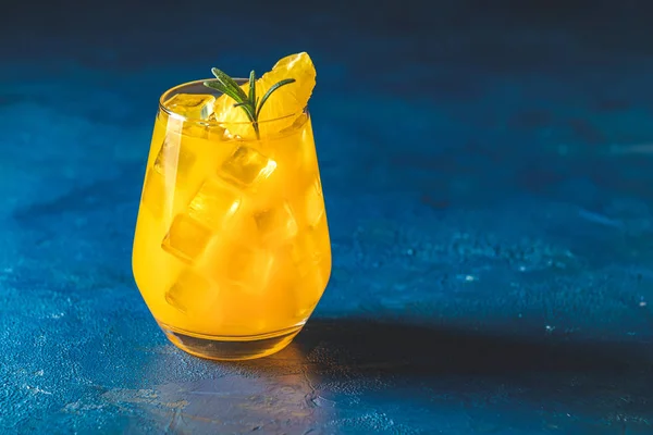 Gelber orangefarbener Cocktail mit Mandarine und Rosmarin mit Eis im Glas auf dunkelblauem Betongrund, Nahaufnahme. Willkommensgetränk für Weihnachten und Neujahr — Stockfoto