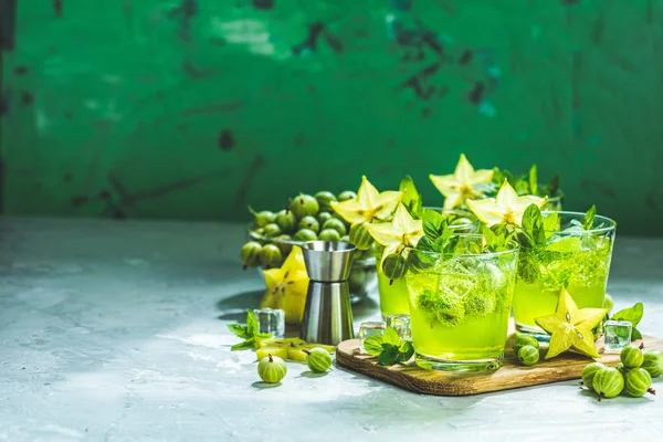 Grüne Stachelbeere und Karambolacocktail mit Likör, Eis und frischer Minze auf einem hellgrauen Betontisch. erfrischendes Sommergetränk, sonniges Licht. oder Entgiftungsgetränk. — Stockfoto