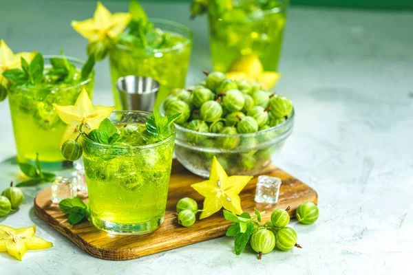 Yeşil bektaşi üzümü ve likör, buz ve açık gri beton masada taze nane ile carambola kokteyl. Serinletici yaz içkisi, güneşli ışık. Ya da detoks içeceği.