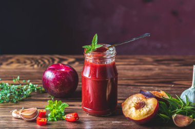 Ev yapımı Diy konserve sıcak erik sosu acı biberli ya da cam kavanozlu tkemali ahşap masada erik, tuz, biber, şifalı otlar ve seçici bir odak noktası ile duruyor.