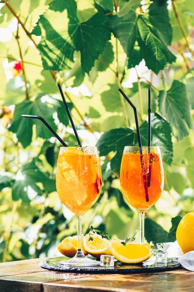 オレンジと大きなワイングラスの中に2つのアペロールスプリッツカクテル、夏のイタリアの新鮮なアルコール冷たい飲み物。ブドウ畑の背景を持つ日当たりの良い庭 — ストック写真